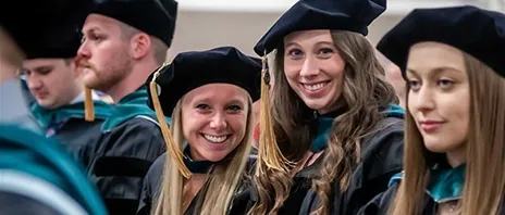 Two newly hooded physical therapy graduates smile at the camera.